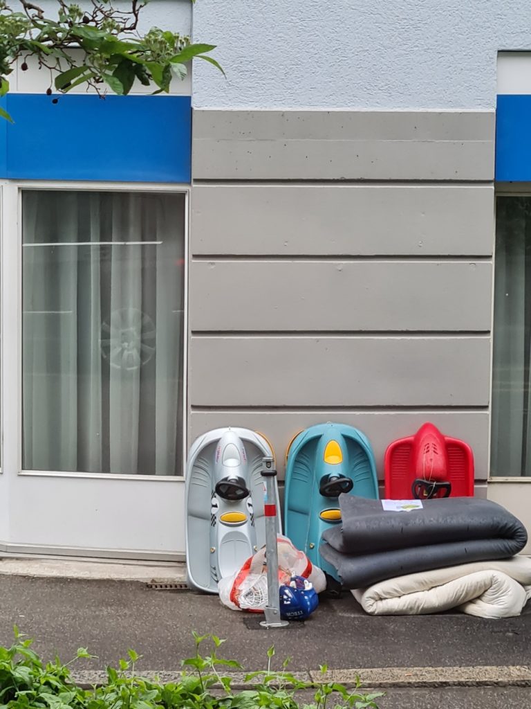 three plastic bobs (silver, red, green) and 2 futon mattresses are lying by the roadside for collection.