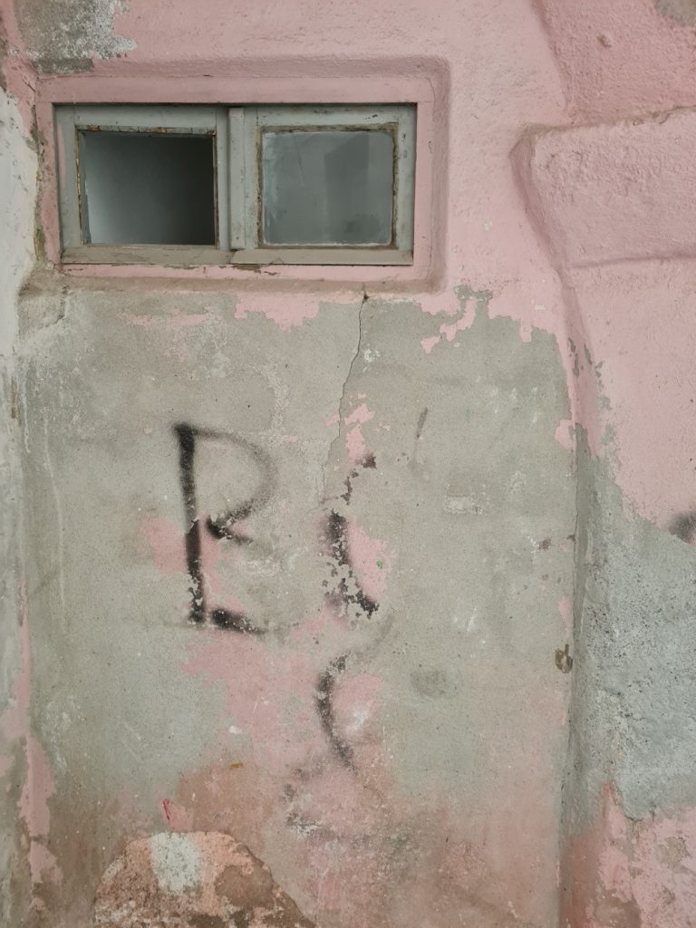 pink house wall (detail) with two almost square, small windows, underneath a lettering starting with ‘B’, then illegible, finale ligure